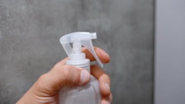 Temiz sprey şişesini tutup tetiği çekerken ince sis spreyini gri arka planda havaya salıyor. Temizlik, dezenfekte ve nemlendirme kavramları