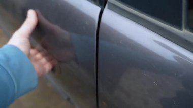 Arızalı bir araba kapısını kapatmaya çalışan hayal kırıklığına uğramış bir insan, ki bu da tekrar tekrar kilitlenemeyip geri sekerek hatalı bir kilit mekanizması ve otomotiv tamirine ihtiyaç olduğunu gösterir.