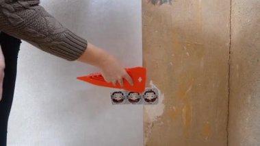 Dişi eller duvarlara yeni duvar kağıtları yapıştırıyor ve bir evin tadilatı sırasında onu turuncu bir spatulayla düzleştiriyor. İç dekorasyon ve tasarım için ev geliştirme ve kendin yap projesi