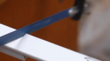 Beyaz plastik bir kablo gövdesini kesen demir testeresinin yakın çekim görüntüsü, atölye ortamındaki testere işlemi sırasında küçük plastik parçacıklar uçuyor.