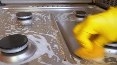 Ev hanımının eli parlak sarı koruyucu bir eldiven içinde kirli paslanmaz bir çelik ocağı köpüklü bir süngerle temizliyor ev işleri yapıyor ve mutfak hijyen bakımını yapıyor.