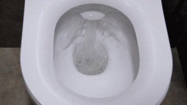 Modern bir banyoda beyaz seramik bir klozetin üzerine sifonu çeken temiz su, hijyen ve temizlik kavramları için güçlü bir girdap sergiliyor. Yıkanmış su dolabının üst görünümü