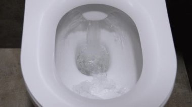 Modern bir banyoda beyaz seramik bir klozetin üzerine sifonu çeken temiz su, hijyen ve temizlik kavramları için güçlü bir girdap sergiliyor. Yıkanmış su dolabının üst görünümü