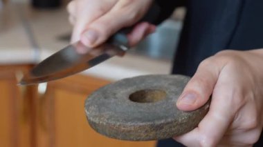 Geleneksel dairesel bir bileme taşı kullanarak metal bir mutfak bıçağını keskinleştirirken bir insanın ellerinin yakın plan görüntüsü yemek hazırlığı için son teknolojiyi geri getiriyor.