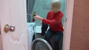 Dikkat et, çamaşırları ayıklayıp modern bir banyodaki ön yükleme makinesine koyarak çamaşırları yıkamaya hazırlanan ev hanımı.