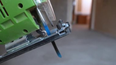 Bıçağı bir aşağı bir yukarı hızla hareket eden yeşil elektrikli bir yapbozun ayrıntılı görüntüsü. Elektrikli alet, ev tadilatı veya inşaat projesi sırasında odun kesmeye hazır