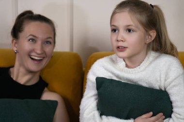 Mutlu anne ve kız evdeki hardal sarısı koltukta dinleniyor, keyifli bir anı paylaşıyor ve sohbet ederken birlikte kaliteli zaman geçiriyorlar.