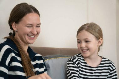 Anne ve kızı evde bir kitabı paylaşırken birlikte gülüyorlar, sıcak bir öğrenme, hikaye anlatma ve rahatlamış aile sevinci hafta sonu tatili boyunca