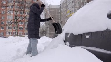 Yoğun kar temizleyen kadın, yoğun kar yağışı alan kadın, kışlık ceketli kadın arabadan ağır kar, eldivenli kadın ve arabasının etrafında kalın kar temizleyen kadın.