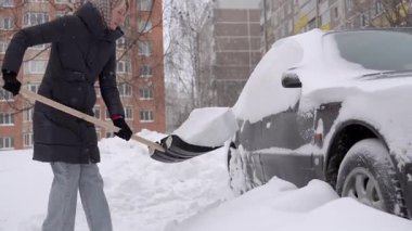 Beyaz kadın araba sakinlerinin yanında kar kürüyor apartmanın önündeki park yerini temizliyor direksiyondan ve geçitten ağır sürükleniyor kışlık kapüşon ve soğuk nefesiyle görünür eldivenler giyiyor.