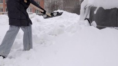 Beyaz kadın araba sakinlerinin yanında kar kürüyor apartmanın önündeki park yerini temizliyor direksiyondan ve geçitten ağır sürükleniyor kışlık kapüşon ve soğuk nefesiyle görünür eldivenler giyiyor.