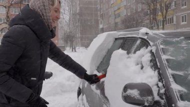 Karları temizleyen kadın, park halindeki arabanın camından karları itinayla kaldıran kadın, kışın fırçayla biriken karı dikkatlice arabadan çıkaran kadın.