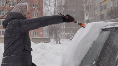 Karları temizleyen kadın, park halindeki arabanın camından karları itinayla kaldıran kadın, kışın fırçayla biriken karı dikkatlice arabadan çıkaran kadın.
