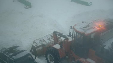 Buzlu park yerini temizleyen ağır makineler, sisli kar yağışı altında çalışan büyük yükleyici, yoğun kış sahnesi, sisli ve buzlu koşullarla çevrili karları temizleyen güçlü bir araç.
