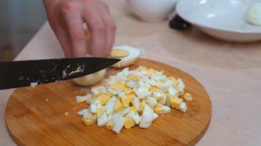 Yumurtalar çabuk doğrandı. Haşlanmış yumurtaları dikkatlice küçük parçalara ayıran ellerin yakınlaşması. Mutfak hazırlığı için yumurta doğrayan elleri olan parlak tezgah ayarı.