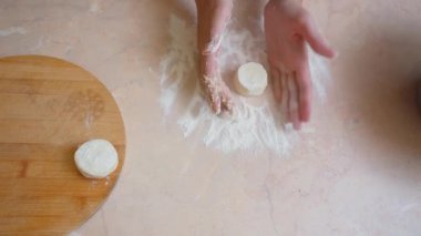 Ekmek hamuru kümelerini ölçüyor ve şekillendiriyor. Pişirme ve düzeltme işlemi için yumuşak hamur parçaları hazırlıyorum. İş yüzeyinde un ile çalışan ve hamur toplarını şekillendiren ellerin yakınlaşması