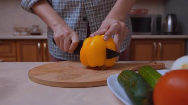 Sebzeler pişti. Salata malzemelerini dilimleme ve dilimleme ile elle hazırlıyorum. Mutfaktaki ahşap bir tahtada sarı dolma biber dilimlerken yakın plan.