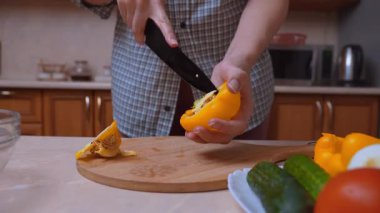 Pişirme hazırlıkları için sarı biber dilimliyorum. Tahta tahtada yemek yapmak için taze sebzeler ayarlandı. Lezzetli ev yapımı yemekler için sarı biberleri dikkatlice dilimleyin.