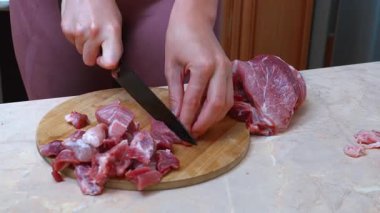Beyaz kadın domuz yağını kesiyor. Yemek pişiren kadın, yuvarlak kesim tahtasındaki domuz etini ustaca dilimliyor. Kadın, hazırlıklar sırasında bıçak kullanarak domuz eti parçalarındaki fazlalıkları dikkatlice temizler.
