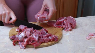 Ahşap tahtaya et doğrayan, yemek pişiren, güveç veya kebap parçaları yapmak için keskin bıçak kullanan, açık mutfak tezgahı ve dikkatli taşıma tekniği kullanan, ahşap panoda et kesen eller.