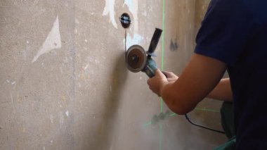 Profesyonel inşaat işçisi, elmas bıçak açı öğütücüsünü kullanarak alçı veya beton bir duvardaki zinciri keserek elektrik tesisatını kuruyor ve yenileme sırasında çok fazla toz yaratıyor.
