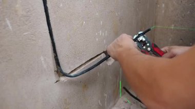 Elektrikçi, Duvar Kanalı 'nın içindeki kondüktörleri aletlerle dikkatlice bağlıyor. Beyaz tenli teknisyen güvenlik kanalı içinde elektrik iletkenlerini titizlikle güvence altına alıyor ve hizalıyor.