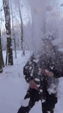 Siyah ceketli ve bereli mutlu genç adam neşe içinde havaya taze toz kar bulutu fırlatıyor, güzel güneşli bir günün tadını çıkarıyor.
