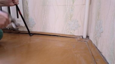 İşçi dikkatlice kaldırır. İşçi Boruların yanındaki süpürgeliği çıkardı. Tadilat sırasında süpürgeliği güvenli bir şekilde sökmek için araç gereç kullanılıyor. İşçi Su Borularının Yanındaki Süpürgeyi Dikkatlice Kaldırmak için Araçları Çalıştırıyor