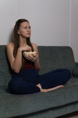 Genç bir kadın rahat bir koltukta oturmuş elinde patlamış mısırla televizyonda sıkıcı bir film seyrediyor ve yüzündeki hayal kırıklığı ve can sıkıntısı ifadesini sergiliyor. Dikey fotoğraf