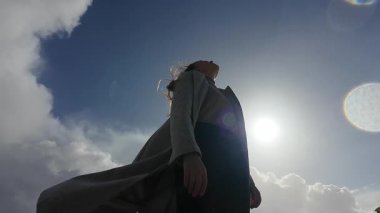 Yanlız bir figür aydınlık bir gökyüzünün altında zarif bir şekilde duruyor, huzuru somutlaştırıyor ve dönen bulutların arasında derin bir yansıma.