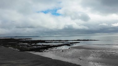 bulutlu gökyüzü altında sakin boş bir sahil, yumuşak yansımaları ve yumuşak gelgitleri olan sakin bir sahil manzarası.