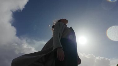 Yanlız bir figür aydınlık bir gökyüzünün altında zarif bir şekilde duruyor, huzuru somutlaştırıyor ve dönen bulutların arasında derin bir yansıma.