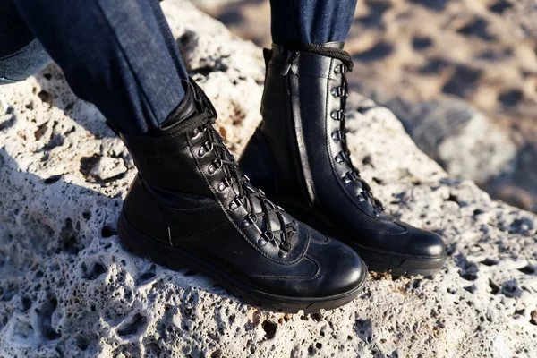 Black eco-leather military boots with laces for active tourism in the forest or mountains on a background of sand and rocks. Caucasus, Russia