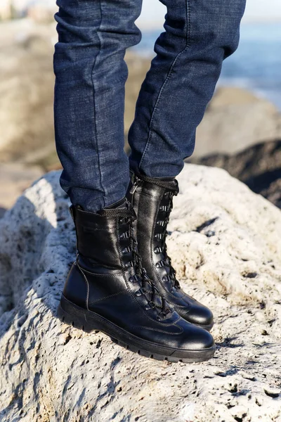 Unisex army black boots in military-style leather on laces for hiking in nature in the forest or mountains on a background of sand and rocks. Caucasus, Russia