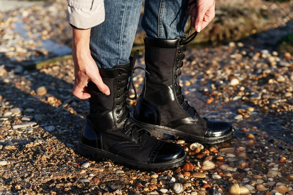Unisex boots of their black leather in an army style with laces for an active tourist holiday on the background of sand and water. Caucasus, Russia