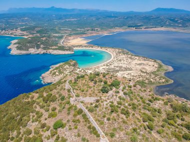 Voidokilia 'nın ünlü yarı dairesel kumlu plajı ve lagününün hava manzarası. Yunanistan 'ın Messenia kentinde kristal berrak turkuaz suyu bulunan Akdeniz' deki en ikonik plajlardan biridir.