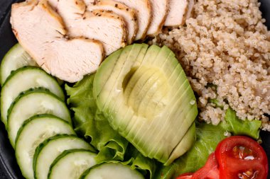 Taze lezzetli salata, kinoa, tavuk ve taze sebzeler, koyu beton bir arka planda.