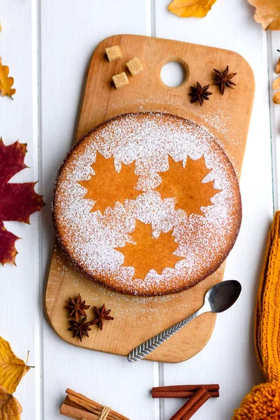 Beautiful fresh sweet pumpkin cake with a maple leaf pattern on a white wooden background with a composition of dry autumn leaves