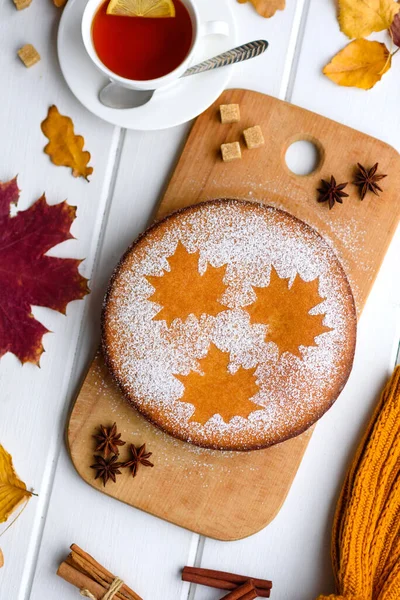 Beautiful fresh sweet pumpkin cake with a maple leaf pattern on a white wooden background with a composition of dry autumn leaves