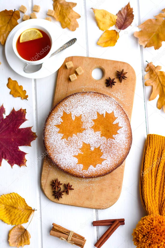 Beautiful fresh sweet pumpkin cake with a maple leaf pattern on a white wooden background with a composition of dry autumn leaves