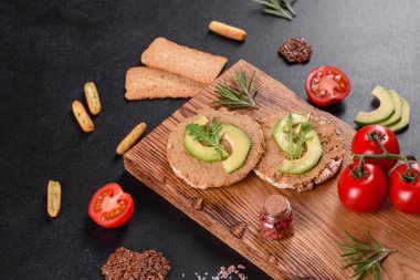 Lezzetli taze sandviç, ciğer ezmesi, avokado parçaları ve koyu beton bir masada roka.