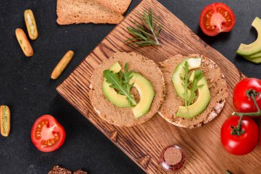 Lezzetli taze sandviç, ciğer ezmesi, avokado parçaları ve koyu beton bir masada roka.