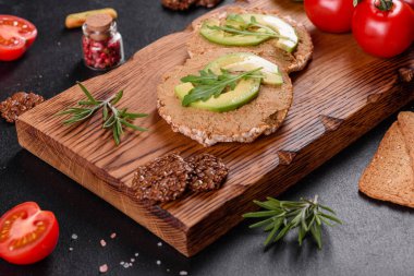 Lezzetli taze sandviç, ciğer ezmesi, avokado parçaları ve koyu beton bir masada roka.