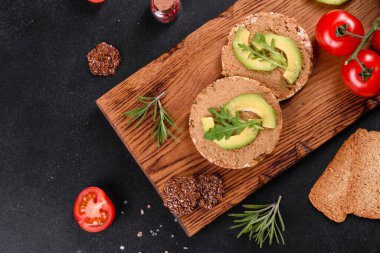 Lezzetli taze sandviç, ciğer ezmesi, avokado parçaları ve koyu beton bir masada roka.