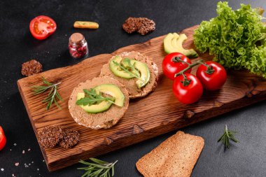 Lezzetli taze sandviç, ciğer ezmesi, avokado parçaları ve koyu beton bir masada roka.