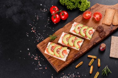 Koyu beton bir masada kırmızı balık, tereyağı, ekmek ve avokado ile nefis taze sandviç.