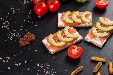 Koyu beton bir masada kırmızı balık, tereyağı, ekmek ve avokado ile nefis taze sandviç.
