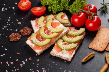 Koyu beton bir masada kırmızı balık, tereyağı, ekmek ve avokado ile nefis taze sandviç.