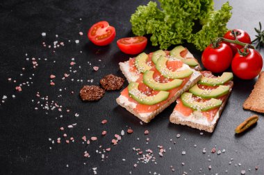 Koyu beton bir masada kırmızı balık, tereyağı, ekmek ve avokado ile nefis taze sandviç.