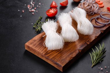 Lezzetli pirinç eriştesi, domates, kırmızı biber, mantar ve deniz ürünleri, koyu beton arka planda.